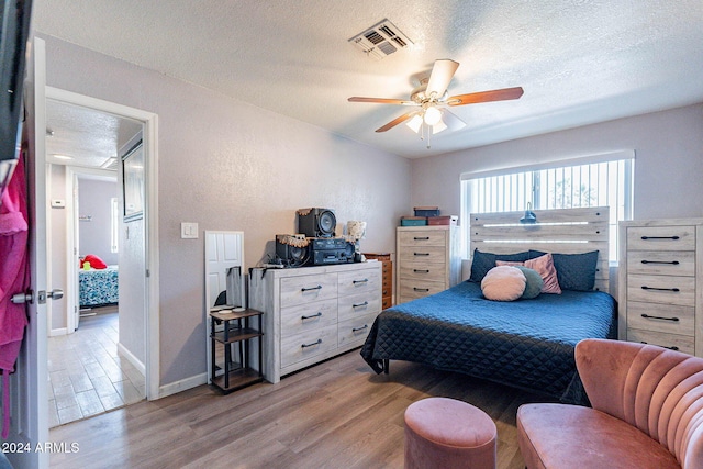 bedroom featuring light hardwood / wood-style flooring, a textured ceiling, and ceiling fan