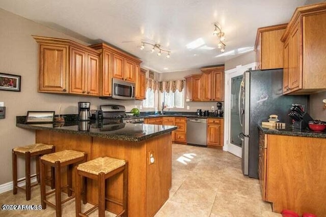 kitchen featuring light tile patterned floors, kitchen peninsula, track lighting, stainless steel appliances, and a breakfast bar