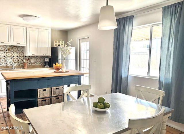 kitchen with a sink, freestanding refrigerator, white cabinets, decorative backsplash, and wooden counters