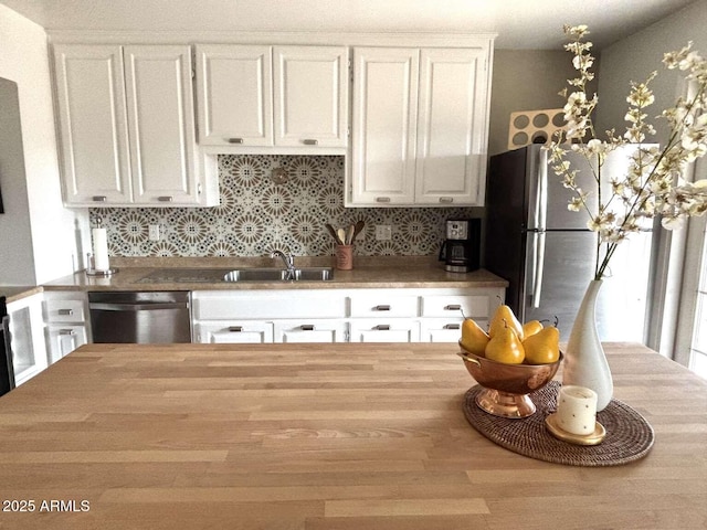 kitchen with backsplash, butcher block counters, appliances with stainless steel finishes, white cabinets, and a sink