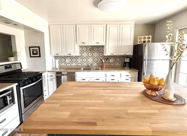 kitchen featuring butcher block countertops, decorative backsplash, stainless steel appliances, white cabinetry, and a sink