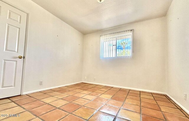 empty room featuring tile patterned flooring, baseboards, and a textured ceiling