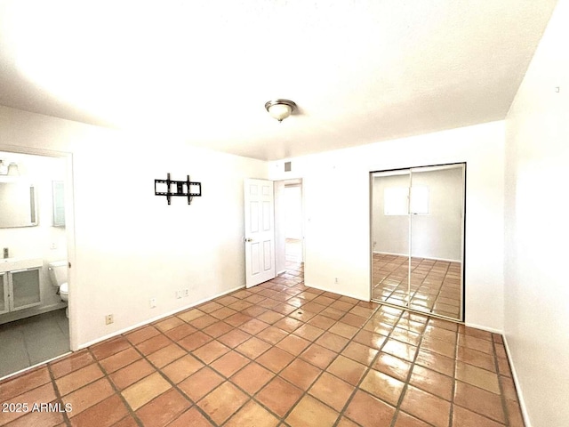 unfurnished bedroom featuring tile patterned floors, visible vents, ensuite bath, a closet, and baseboards