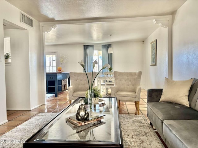 living area featuring tile patterned floors, visible vents, a textured ceiling, and a wealth of natural light