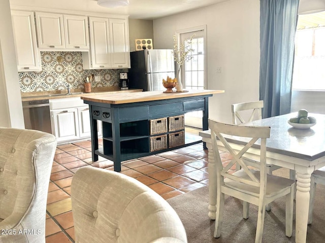 kitchen with light tile patterned floors, butcher block countertops, stainless steel appliances, white cabinets, and tasteful backsplash