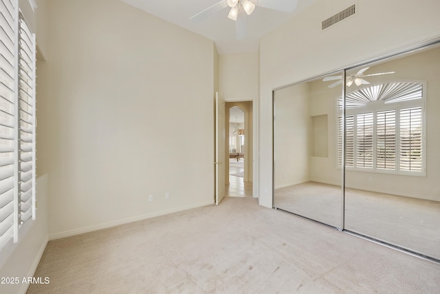 unfurnished bedroom with ceiling fan, a closet, light carpet, and a towering ceiling