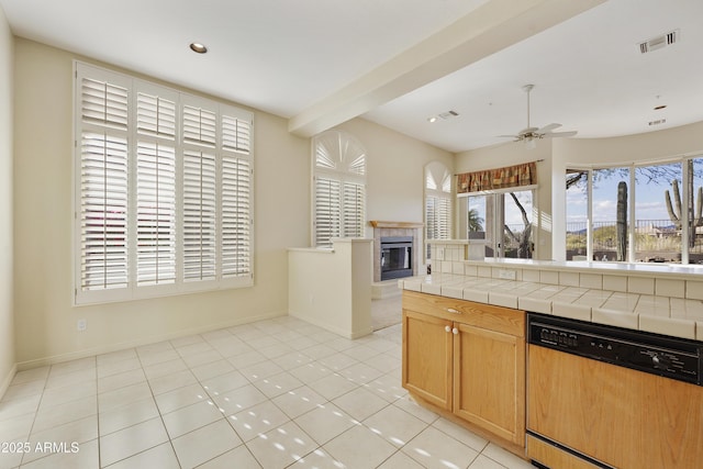 kitchen featuring light tile patterned floors, tile counters, dishwasher, ceiling fan, and a tiled fireplace