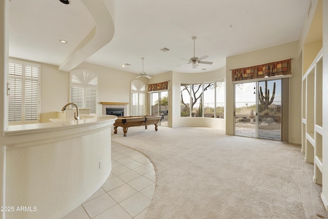 interior space with sink, ceiling fan, a tiled fireplace, beam ceiling, and light carpet