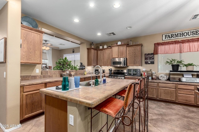 kitchen featuring ceiling fan, sink, a kitchen bar, a kitchen island with sink, and appliances with stainless steel finishes