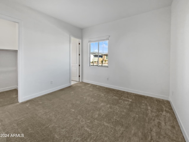 unfurnished bedroom with dark colored carpet, a walk in closet, and a closet