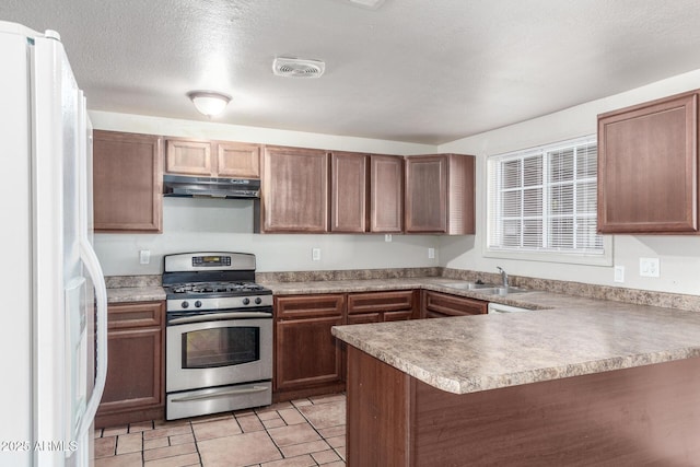 kitchen with sink, stainless steel gas stove, a textured ceiling, kitchen peninsula, and white refrigerator with ice dispenser