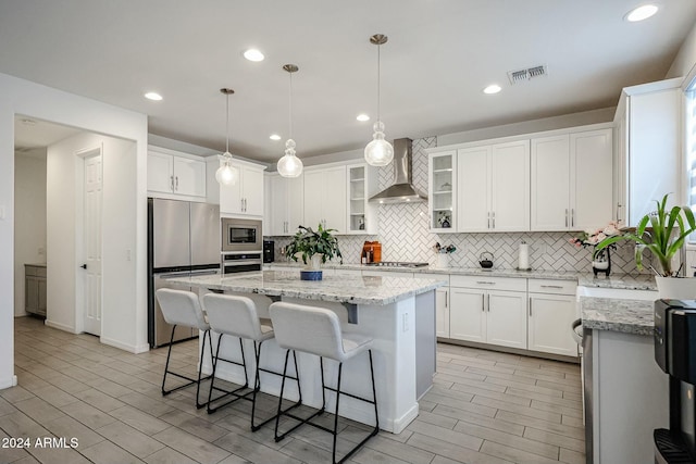 18813 W Solano Dr, Litchfield Park, AZ 85340 - kitchen with stainless steel appliances, wall chimney exhaust hood, backsplash, a kitchen bar, and a center island