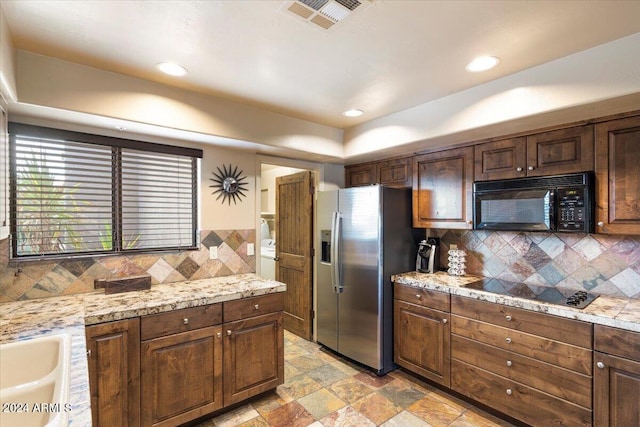 kitchen featuring black appliances, light stone countertops, dark brown cabinetry, and tasteful backsplash