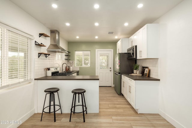 kitchen featuring open shelves, dark countertops, white cabinetry, stainless steel appliances, and wall chimney exhaust hood