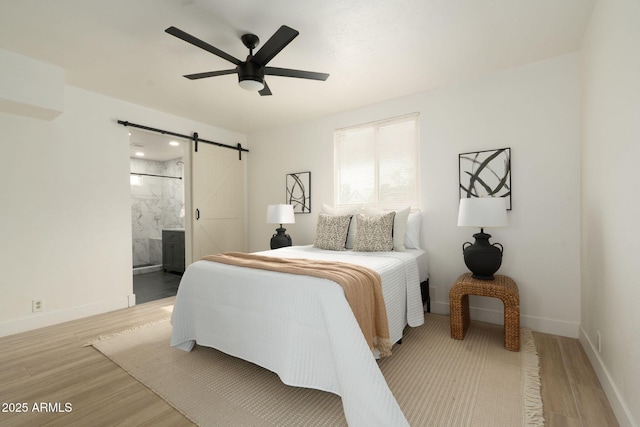 bedroom featuring connected bathroom, a barn door, baseboards, and wood finished floors