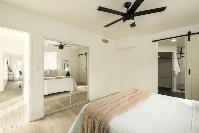 bedroom featuring visible vents, wood finish floors, ceiling fan, a barn door, and a closet