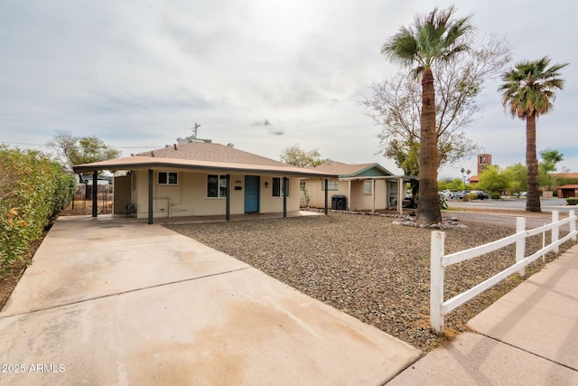 view of front of property featuring an attached carport, fence, central AC, stucco siding, and concrete driveway