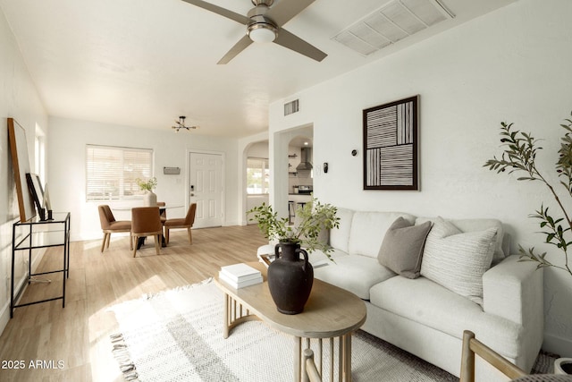 living room with visible vents, arched walkways, light wood-style floors, and a ceiling fan