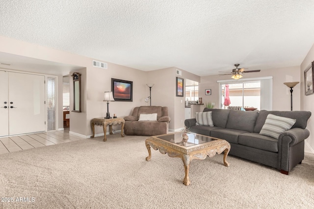 carpeted living area featuring a textured ceiling, ceiling fan, tile patterned flooring, visible vents, and baseboards