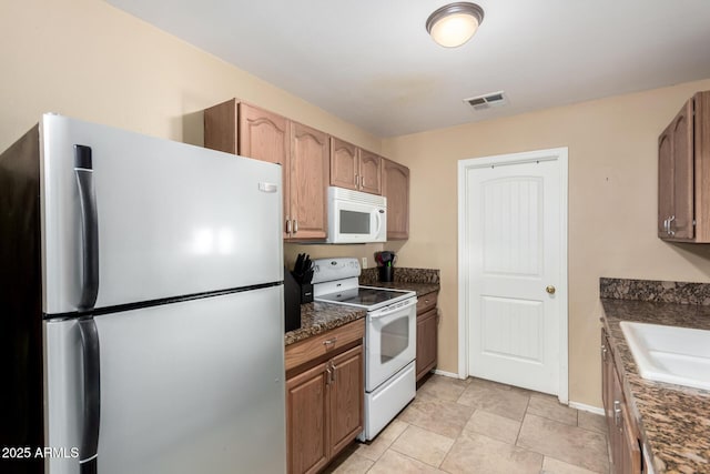 kitchen featuring dark stone countertops, sink, light tile patterned floors, and white appliances