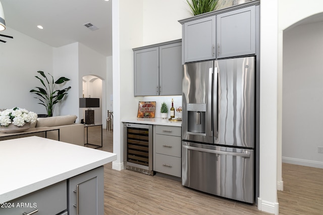 kitchen with beverage cooler, stainless steel fridge, light hardwood / wood-style floors, and gray cabinetry