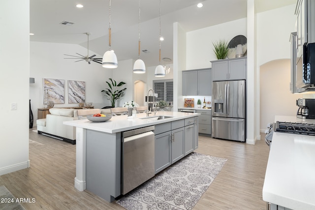 kitchen with sink, a kitchen island with sink, light hardwood / wood-style flooring, high vaulted ceiling, and appliances with stainless steel finishes