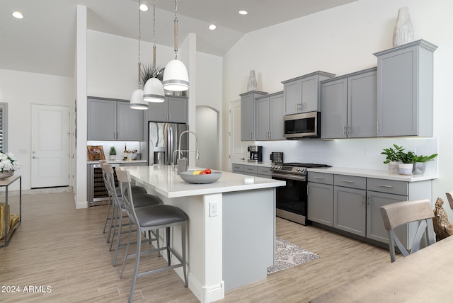 kitchen featuring beverage cooler, a breakfast bar area, decorative light fixtures, stainless steel appliances, and high vaulted ceiling