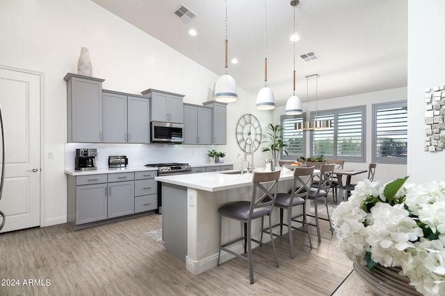 kitchen featuring stainless steel appliances, gray cabinetry, pendant lighting, a breakfast bar area, and light hardwood / wood-style flooring