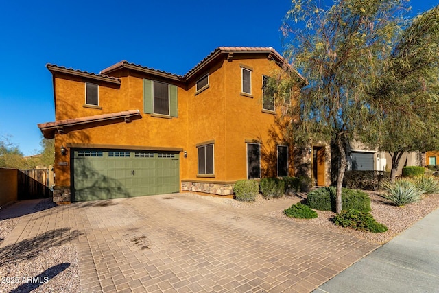 view of front of house featuring stone siding, an attached garage, fence, decorative driveway, and stucco siding