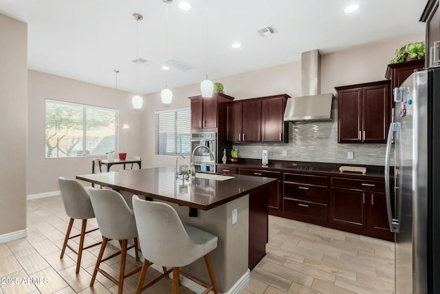 kitchen featuring wall chimney range hood, hanging light fixtures, stainless steel fridge, an island with sink, and black cooktop