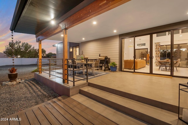 deck at dusk with outdoor dining space, a patio area, fence, and an outbuilding