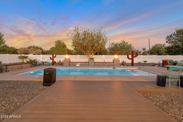 pool at dusk with a wooden deck, a patio, a fenced backyard, and a fenced in pool