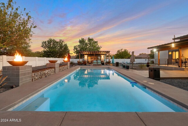 pool at dusk with a patio area, a fenced backyard, and a pergola