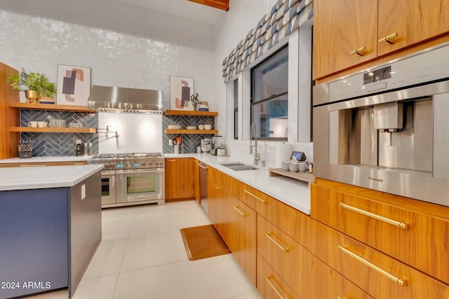 kitchen with open shelves, light countertops, appliances with stainless steel finishes, a sink, and wall chimney range hood