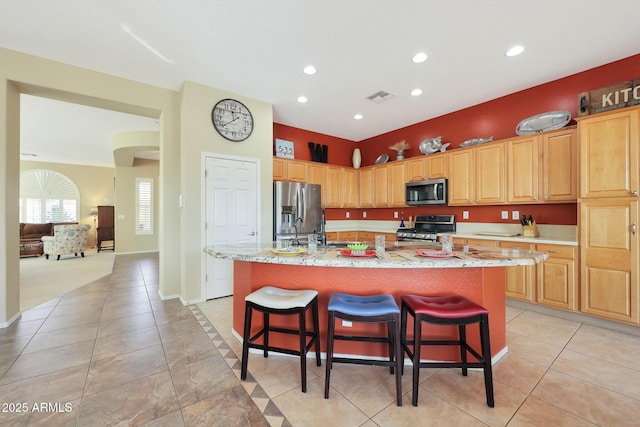 kitchen featuring a kitchen bar, light tile patterned floors, stainless steel appliances, and a kitchen island with sink