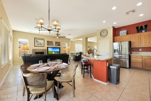 dining area with ceiling fan with notable chandelier, sink, light tile patterned floors, and a tiled fireplace