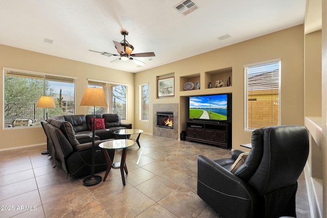 living room with ceiling fan, a wealth of natural light, built in features, and a tile fireplace