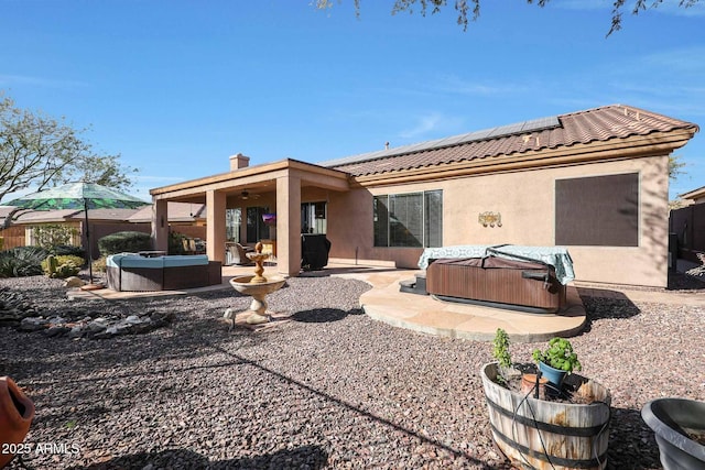 back of house with a hot tub, solar panels, and a patio