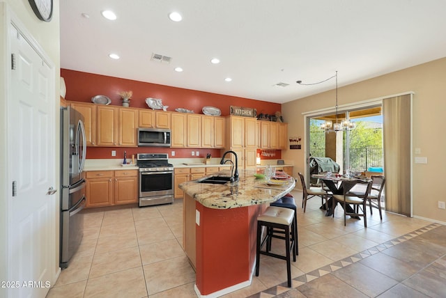 kitchen with appliances with stainless steel finishes, decorative light fixtures, an island with sink, sink, and light tile patterned floors