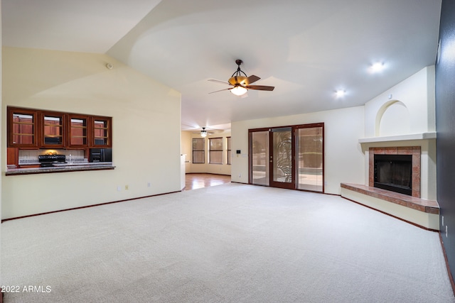 unfurnished living room with a tile fireplace, vaulted ceiling, ceiling fan, and light carpet