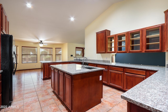 kitchen featuring sink, light tile flooring, a kitchen island with sink, and black fridge