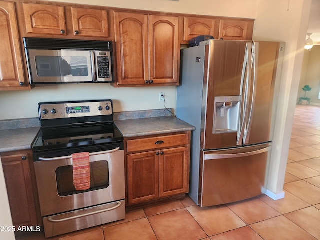 9939 W Ironwood Dr, Sun City, AZ 85351 - kitchen featuring stainless steel appliances, light tile patterned floors, brown cabinetry, and dark countertops