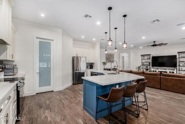 kitchen with white cabinetry, an island with sink, decorative light fixtures, a breakfast bar, and appliances with stainless steel finishes