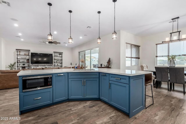 kitchen with pendant lighting, ceiling fan, stainless steel microwave, and blue cabinetry