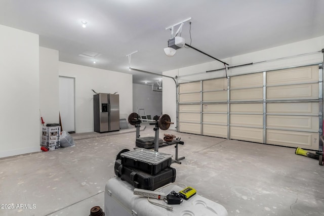 garage with a garage door opener and stainless steel refrigerator with ice dispenser