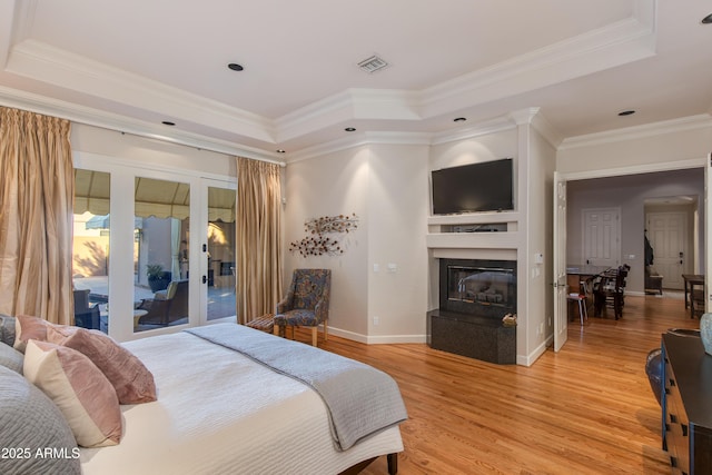 bedroom with crown molding, a raised ceiling, light hardwood / wood-style floors, and french doors