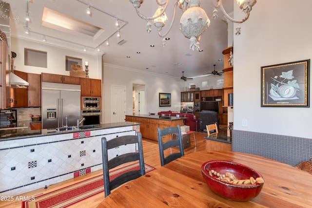 dining area with crown molding, sink, ceiling fan with notable chandelier, and light hardwood / wood-style floors