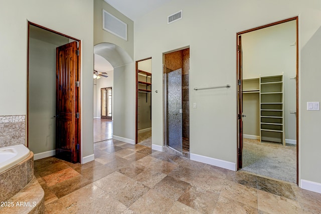 hall with arched walkways, stone finish floor, visible vents, and baseboards