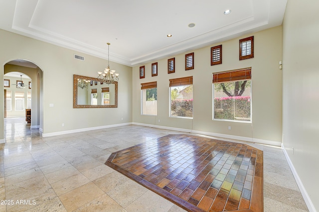 empty room featuring arched walkways, a raised ceiling, visible vents, and baseboards