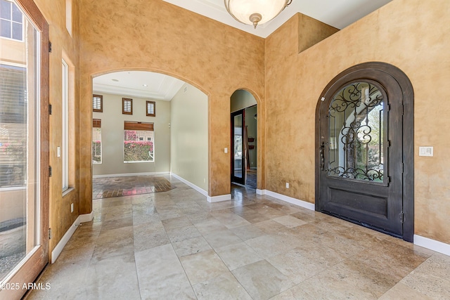 foyer entrance featuring arched walkways, baseboards, and a high ceiling